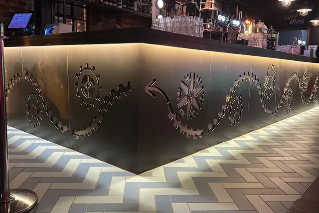 Bespoke laser-cut steel panelling wrapping a bar counter in a Liverpool venue fit-out