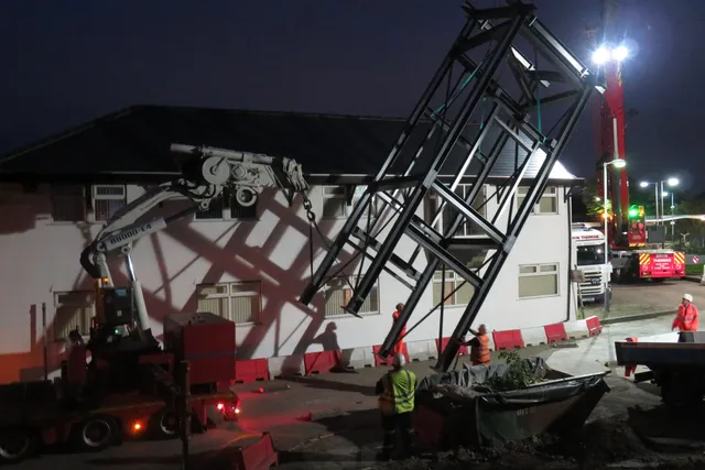 Steel footbridge being lifted into place by crane during a night possession