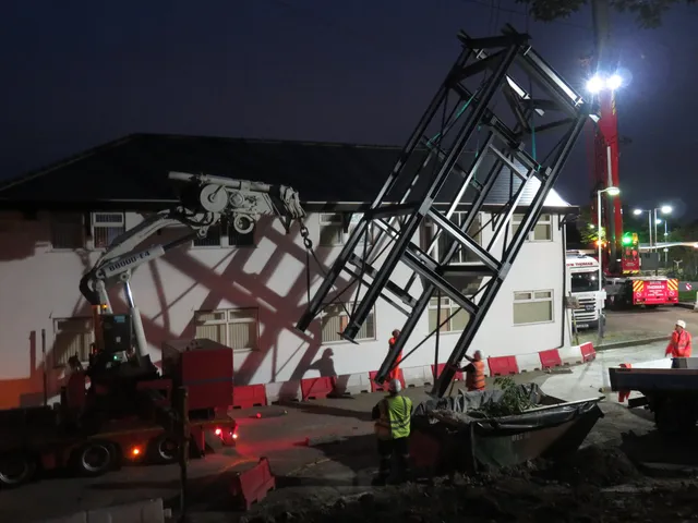 Steel footbridge being lifted into place by crane during a night possession