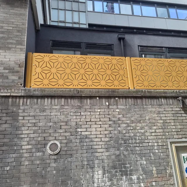 Perforated gold screen panels fixed to a brick boundary wall