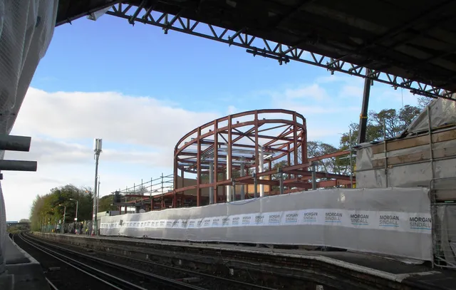Curved red steel arch structure erected over a station platform
