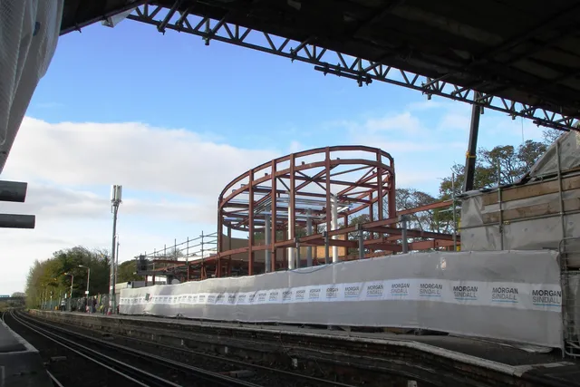 Curved red steel arch structure erected over a station platform