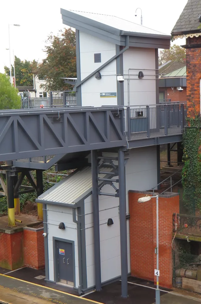 Accessible lift tower and steel footbridge landing at a Merseyrail station