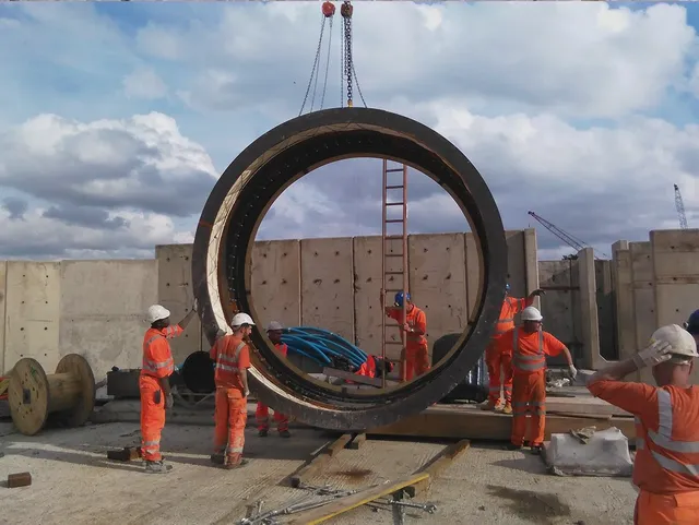 Crew handling a large steel tunnel ring segment on site