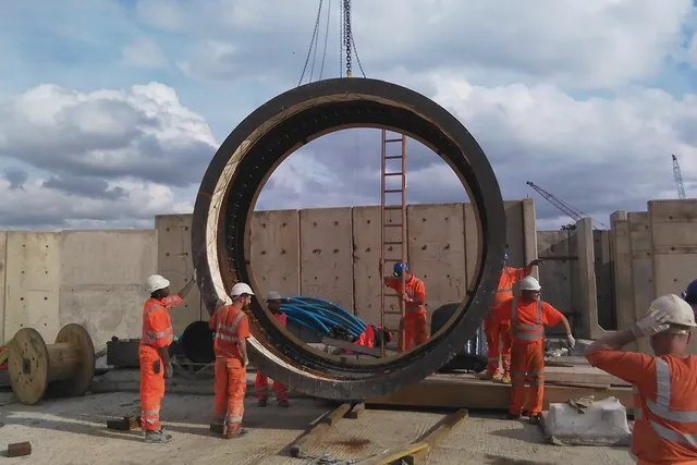 Crew handling a large steel tunnel ring segment on site